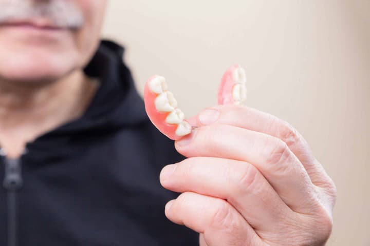 Close-up of removable dental bridge held by senior male patient